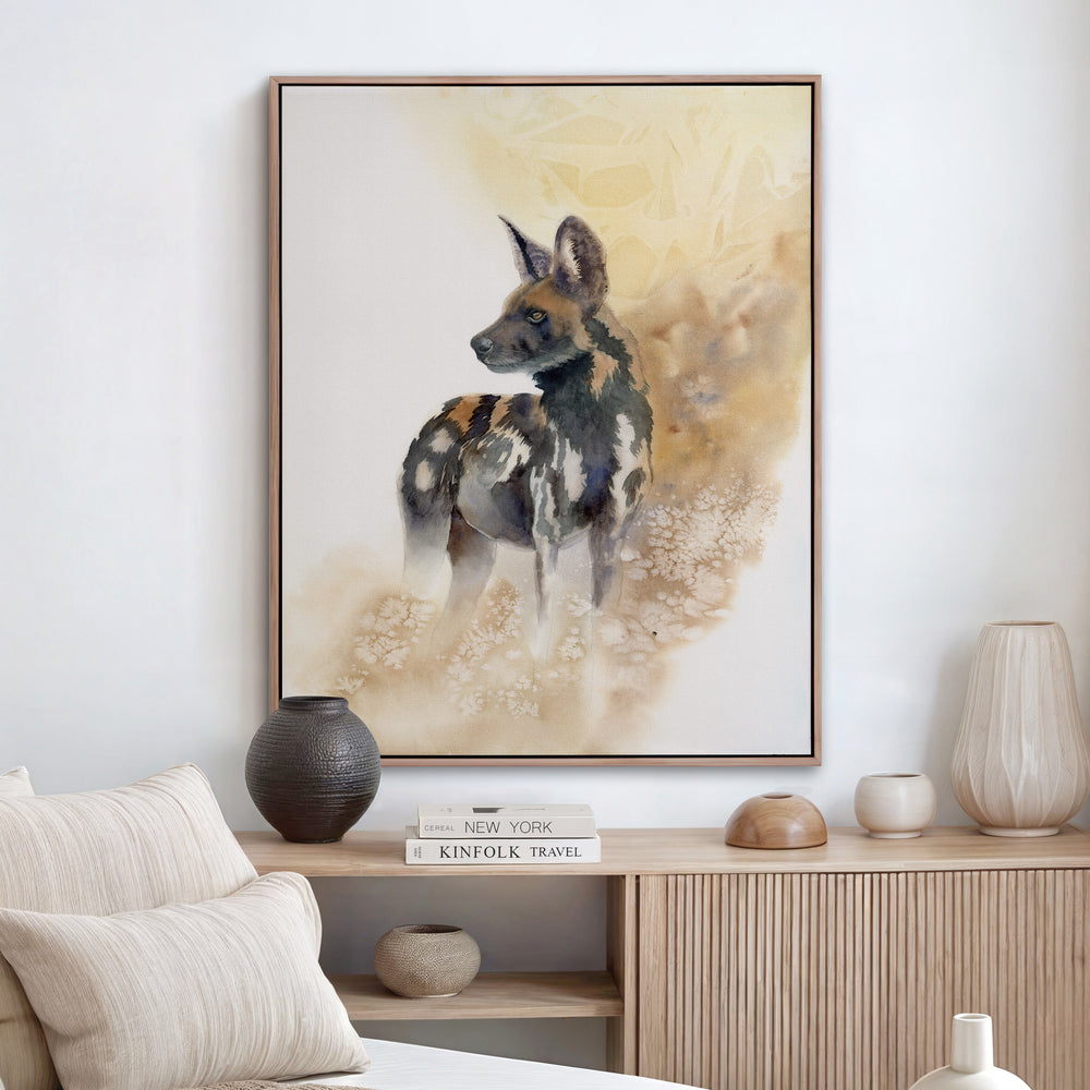 Watercolor painting of an endangered African wild dog standing alert, rendered in rust, black, and gold against a warm dissolving amber background.