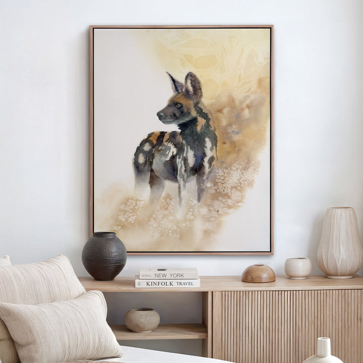 Watercolor painting of an endangered African wild dog standing alert, rendered in rust, black, and gold against a warm dissolving amber background.