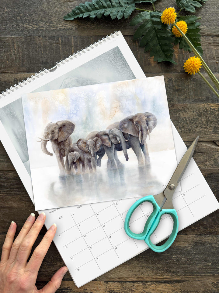 Frame-ready elephant watercolor print being cut with scissors from the 2027 wildlife calendar